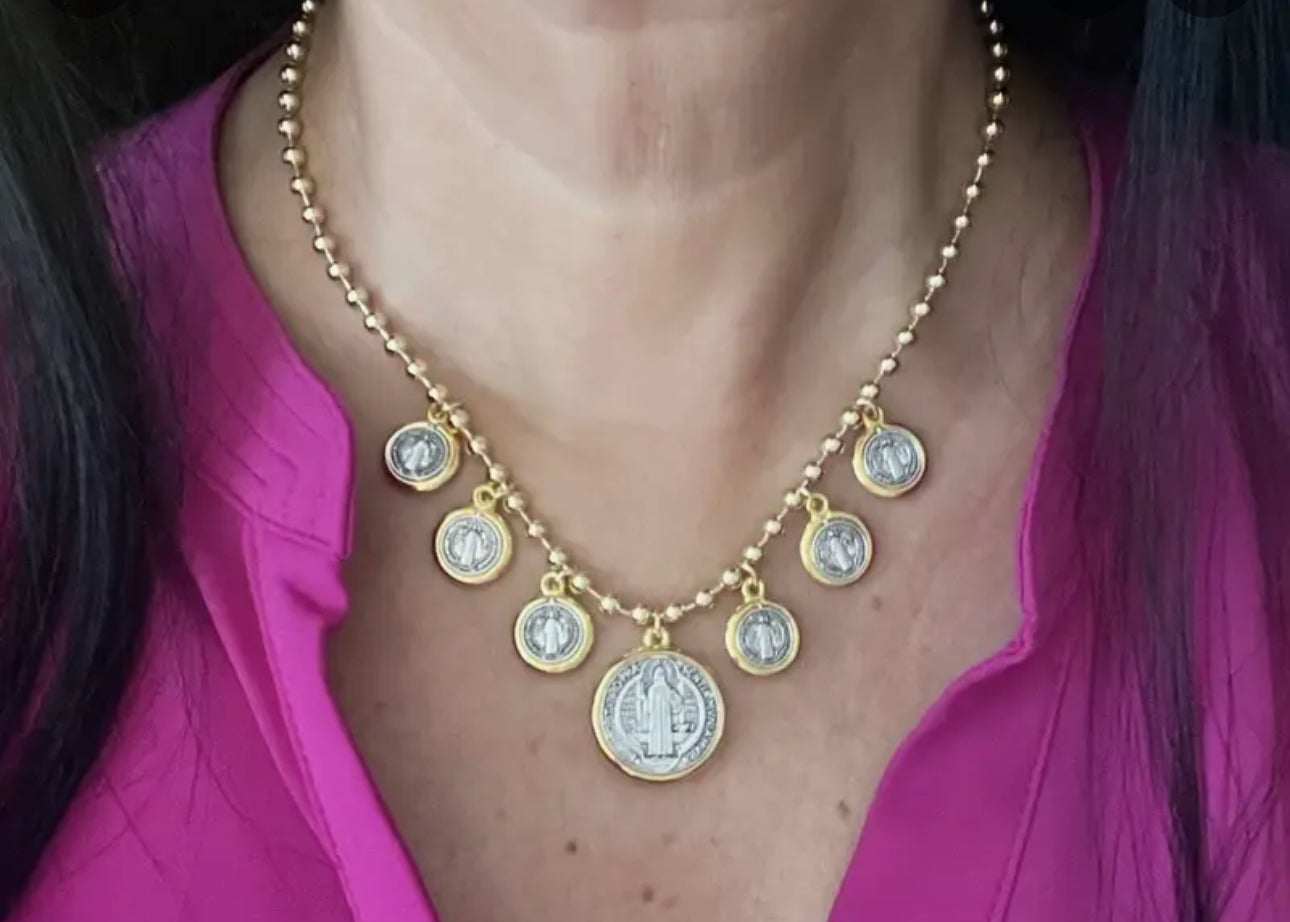 This bold necklace features a gold-toned beaded chain adorned with seven medallion charms of Saint Benedict.