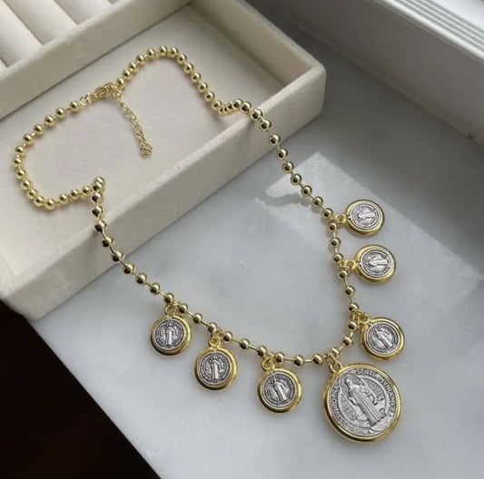 This bold necklace features a gold-toned beaded chain adorned with seven medallion charms of Saint Benedict.